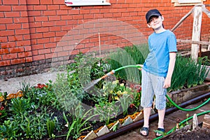 Cheerful boy watering flowers in the garden