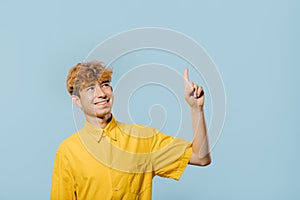 Cheerful boy in yellow shirt pointing up direction on blue background, photo