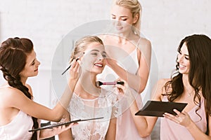 Cheerful bridesmaids helping the bride to get ready