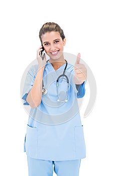 Cheerful brown haired nurse in blue scrubs making a phone call and raising her thumb