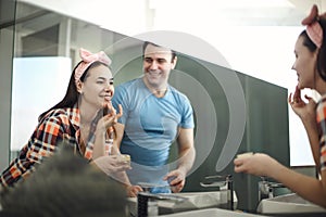 Cheerful brunette man looking at beautiful girlfriend applying face cream in bathroom