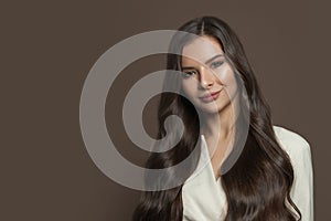 Cheerful brunette model woman with long healthy hair smiling on brown background, fashion beauty portrait