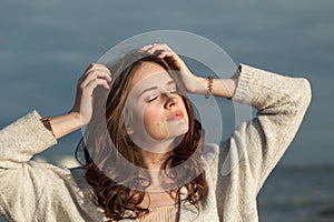 Cheerful brunette woman with fresh skin, natural make-up and healthy wavy brown hair enjoying the sunny morning and sea air.