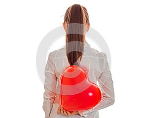 Cheerful brunette woman in love posing from behind with red heart baloon in her hands isolated on white background