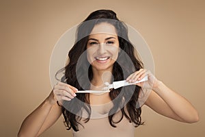 Cheerful brunette young woman holding teeth brush and toothpaste