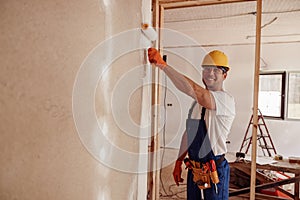 Cheerful builder painting wall in house under construction