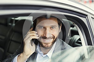 Cheerful business man on mobile phone in rear of the car. Lookin
