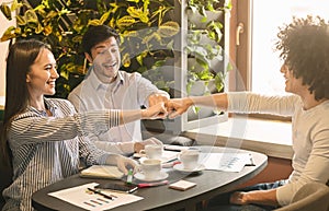 Cheerful business partners making fist bump in cafe