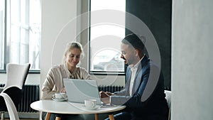 Cheerful business partners man and woman talking and using laptop in modern cafe