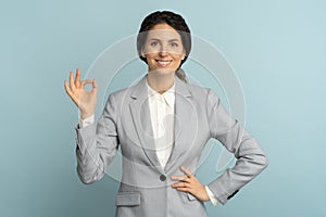 Cheerful business woman wear blazer in good mood smiling broadly, showing okay gesture in studio.