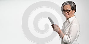 Cheerful business woman works on digital tablet on white background. Mature lady in white looking at camera. Horizontal