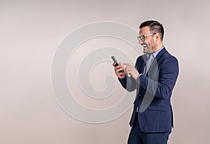 Cheerful businessman in eyeglasses laughing and text messaging over smartphone on white background