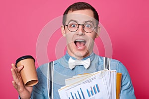 Cheerful businessman has great idea whil having resting and drinking coffee from paper cup. Handsom Caucasian guy wears blue shirt