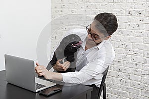 Cheerful businessman and his cute dog pug working on laptop at home