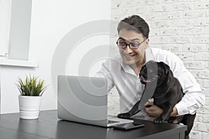 Cheerful businessman and his lovely pet pug working on laptop at home. Distant work and friendship concepts