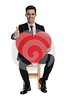 Cheerful businessman holding a heart shape and giving thumbs up