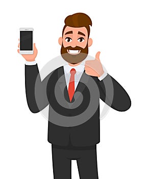 Cheerful businessman holding/showing brand new smartphone/mobile/cell phone in hand and gesturing thumbs up sign. Good, deal.