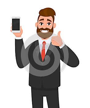 Cheerful businessman holding/showing brand new smartphone/mobile/cell phone in hand and gesturing thumbs up sign. Good, deal. photo