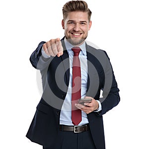 Cheerful businessman pointing and holding his phone