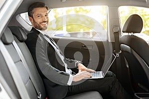 Cheerful businessman working on laptop while going to airport