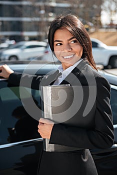 Cheerful businesswoman with folder near black car