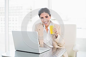 Cheerful businesswoman with laptop and glass of orange juice at