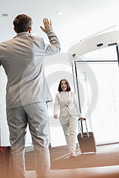 Cheerful businesswoman with luggage walking towards male colleague in convention center