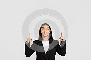 Cheerful businesswoman pointing upwards with both hands at free space