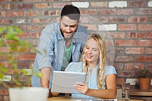 Cheerful businesswoman showing digital tablet to colleague