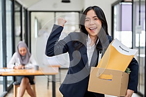 A cheerful businesswoman is showing her fist and carrying a cardboard box, happy to quit her job