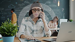 Cheerful businesswoman speaking on mobile phone discussing work in open space office