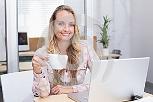 Cheerful businesswoman using her notebook holding a cup