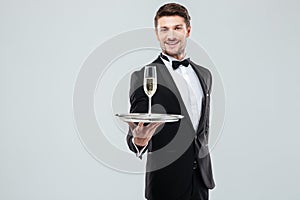 Cheerful butler in tuxedo offering you glass of champagne