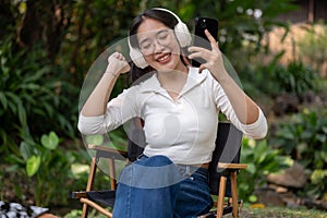 A cheerful and carefree Asian woman is enjoying the music on her headphones while sitting outdoors