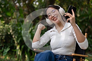 A cheerful and carefree Asian woman is enjoying the music on her headphones while sitting outdoors