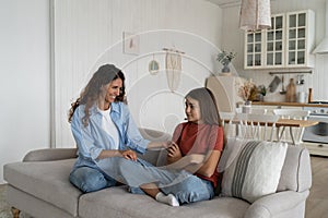 Shy introverted teenage girl sits in closed position on couch with mother wanting to play together photo