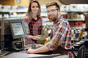 Cheerful cashier man on workspace in supermarket shop.