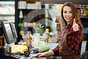 Cheerful cashier woman on workspace showing thumbs up. photo