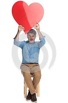 Cheerful casual man holding a heart shape above his head