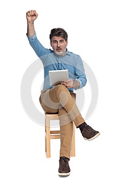 Cheerful casual man holding his tablet and celebrating