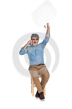 Cheerful casual man talking on phone and holding speech bubble