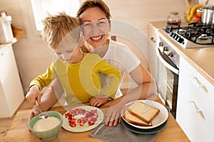 cheerful Caucasian blond mother and child son are sitting in the kitchen and eating. happy childhood and motherhood
