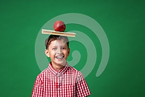 Cheerful Caucasian boy holds his school books and a green Apple on his head