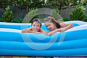 Cheerful Caucasian children, brothers and sisters swim in the inflatable pool and smile cutely, looking at the camera