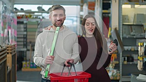 Cheerful Caucasian couple dancing and singing holding shopping basket and tools. Portrait of joyful happy man and woman