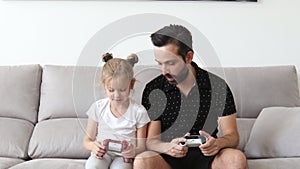 Cheerful Caucasian father playing videogames emotionally together with his cute daughter winning