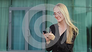 Cheerful Caucasian female student sitting outdoor blonde young woman using telephone, take break holding mobile phone