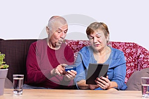 Cheerful caucasian grey senior couple purchasing new furniture online, using credit card and digital tablet, just moved