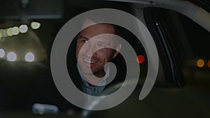 Cheerful Caucasian man driving his car in the evening and smiling in good mood. Smiled guy traveling in car. Close up of