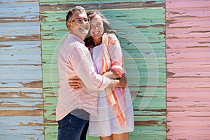 Cheerful caucasian senior couple embracing and looking away while standing against wooden wall